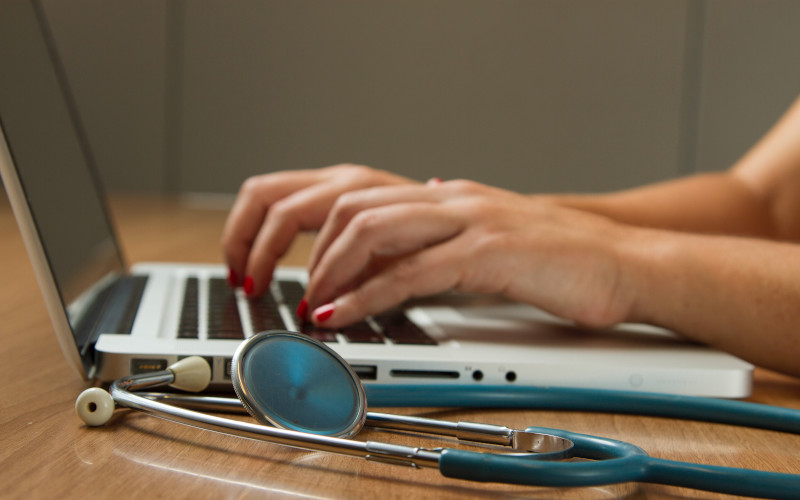 Laptop and stethoscope 800x500 Person typing on a laptop with a stethoscope on the desk